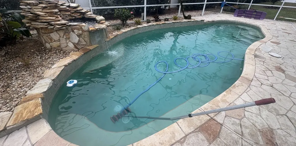 Pool with cleaning brush within surrounded by rock tile landscaping